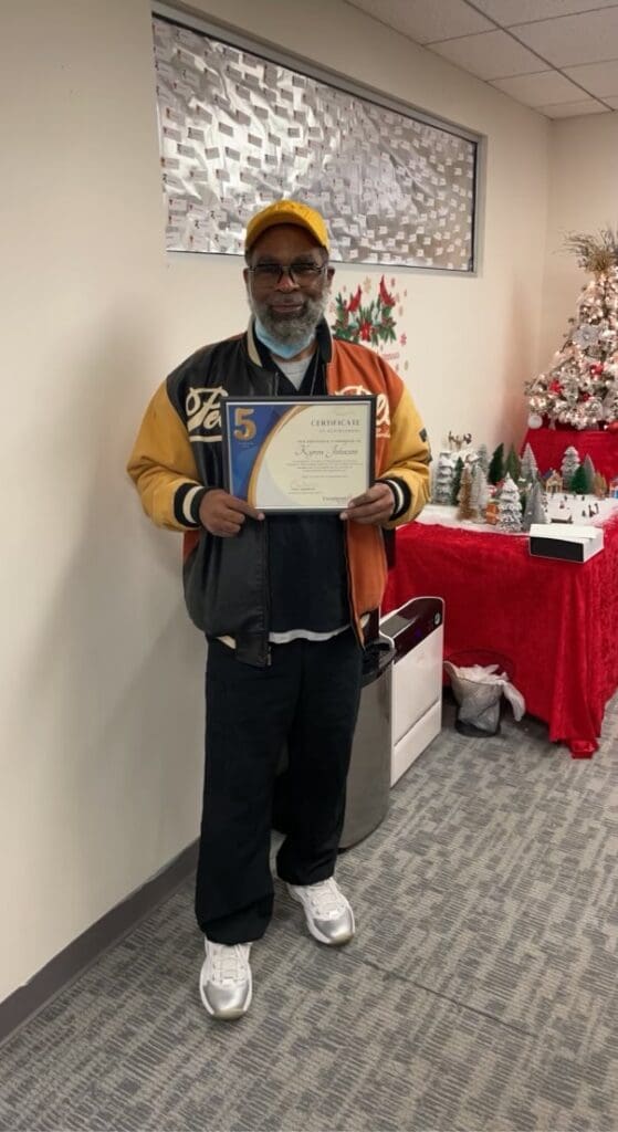 A man holding up his certificate in front of a christmas tree.